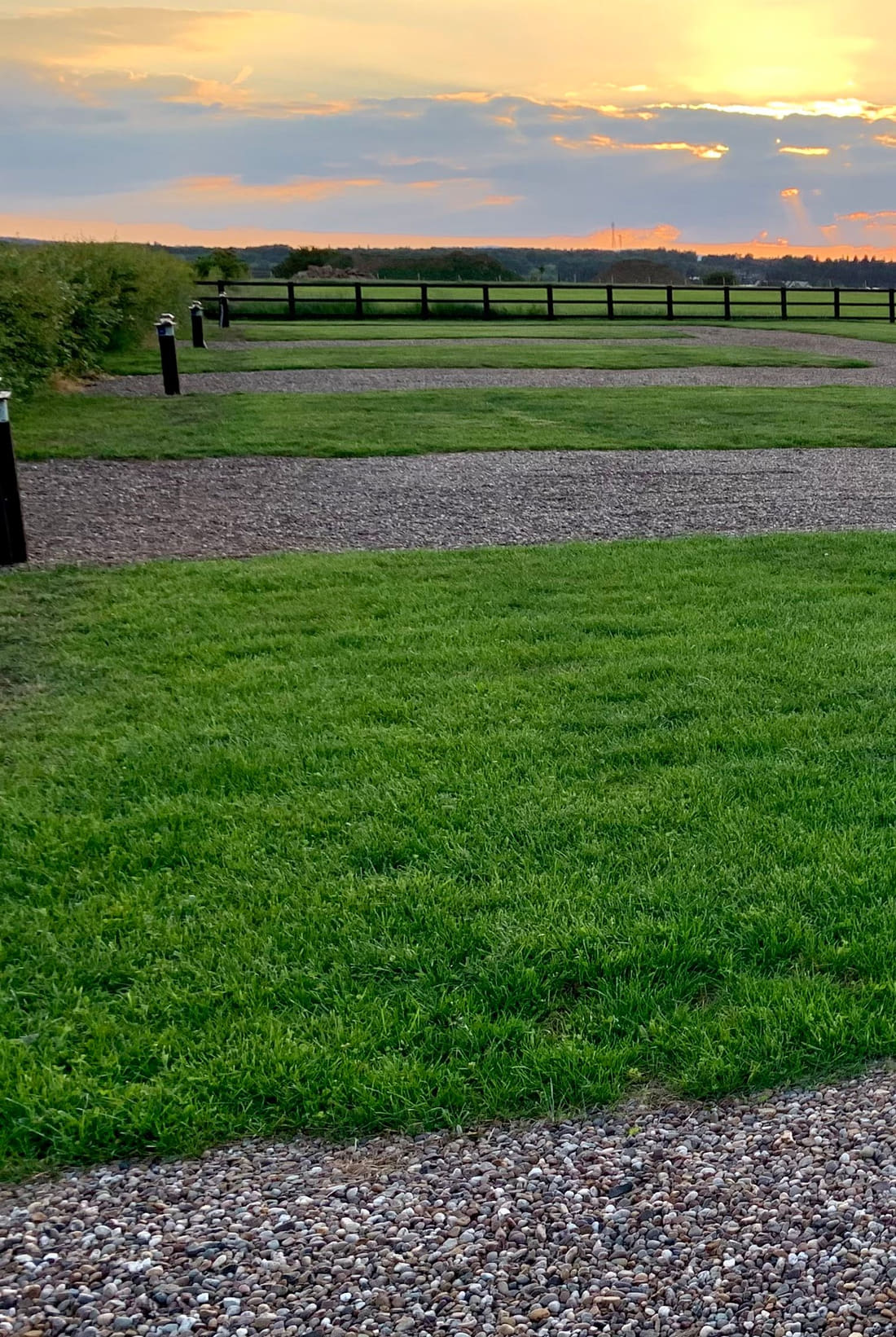 Sunset over the pitching area, with a gravel bay, mown grass and two black timber hook up posts catching the last light.